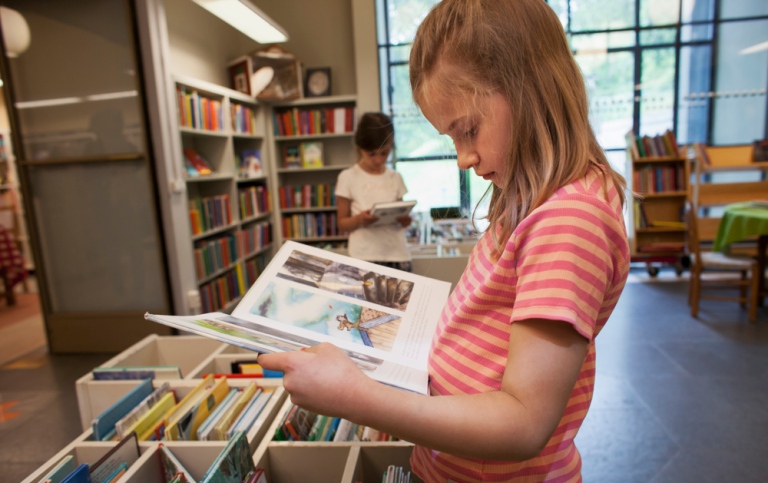 Flicka läser bilderbok i bibliotek